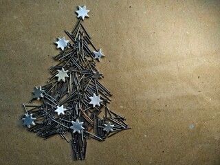 christmas tree folded from construction nails decorated silver stars on kraft paper background.