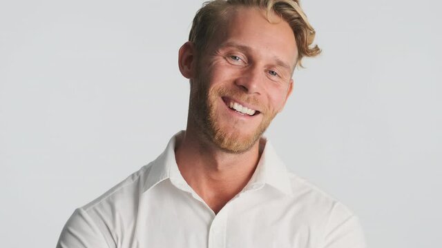 Attractive blond man touch his beard happily looking in camera over white background