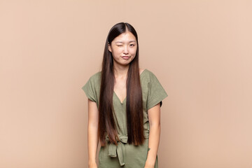 asian young woman looking happy and friendly, smiling and winking an eye at you with a positive...