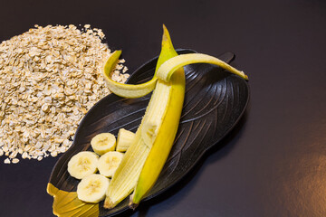 fresh banana and slices and whole oats grains on black background