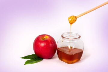 Glass jar with honey and a wooden stick on a purple background. Pouring aromatic honey into jar, close up.  Space for text or design.