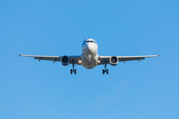 Airplane with chassis from the front landing or taking off on the background of clear blue sky