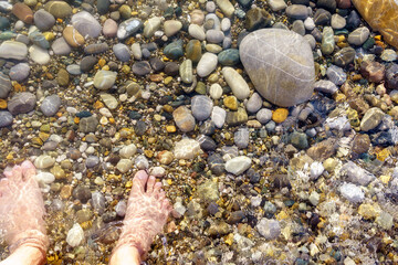 Close up view of a man feet into the pebbles on the beach with sea water flowing