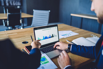 Cropped image of male and female experts browsing business infographics laptop computer for discussing productivity of strategy, skilled traders checking web graphic charts via app on netbook