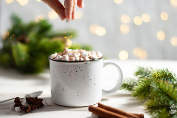 Christmas white cup with hot chocolate and marshmallows on with cinnamon sticks with beautiful garland lights