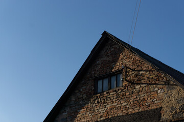 Very old brick house with a small window in the attic against the blue sky.