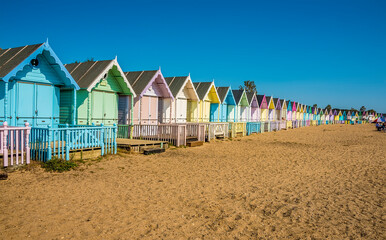 A wide-angle view along brightly coloured beach huts on West Mersea beach, UK in the summertime - Powered by Adobe