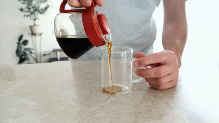 Man pours a freshly brewed coffee into a glass cup from the glass server. Pourover, V60.