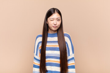 asian young woman looking happy and friendly, smiling and winking an eye at you with a positive...