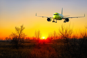 A bright red sunset and a big jet landing on the background of orange sky.