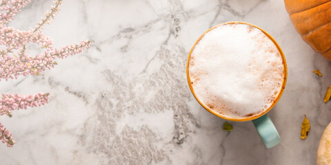 Autumn moody background with mug of latte coffee and pumpkins on marble table. Banner