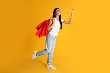 Fototapeta na wymiar Beautiful young woman with paper shopping bags on yellow background