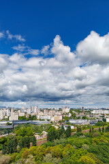An urban landscape with a green park, residential areas and a TV tower against a bright blue sky with thickening clouds.