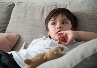 Child putting finger in his mouth.Schoolboy biting his finger nails while watching TV, Emotional kid portrait, Young boy siting on sofa looking out with thinking face or nervous, Children Health care 