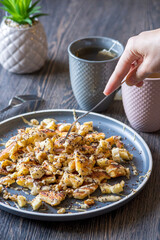 A hand grabbing with a fork a gluten-free, shredded pancake / kaiserschmarrn served with halvah spread, banana, walnuts, and grated chocolate placed on a decorative plate and teacups at the background