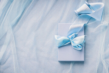Gift boxes with hand dyed silk ribbon with bow on wood spool on blue fabric with folds background and copy space