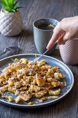 A hand grabbing with a fork a gluten-free, shredded pancake / kaiserschmarrn served with halvah spread, banana, walnuts, and grated chocolate placed on a decorative plate and teacups at the background