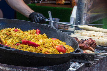 Healthy street food to go - in a large cauldron hot pilaf with pieces of meat and whole hot red pepper. Delicious food cooked over an open fire, which is offered at a street food fair, event, festival