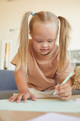 Vertical portrait of cute blonde girl with down syndrome drawing or writing during development...