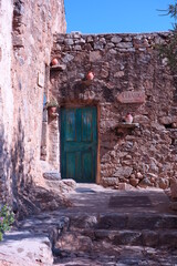 Fototapeta na wymiar Wunderschöne grüne Tür mit historischer Steinmauer Blumentöpfen und blauem Himmel