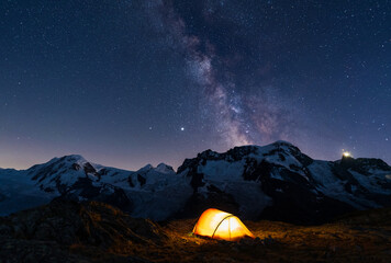 lluminated tent high in the mountains under the night sky with the milky way.