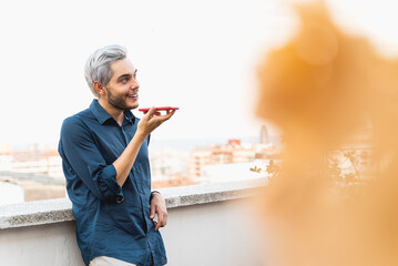 Happy guy talking over smart phone using voice notes outdoors - Focus on face
