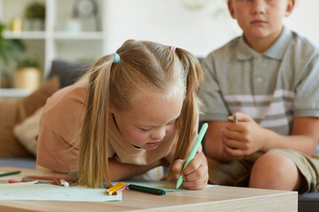 Portrait of cute blonde girl with down syndrome writing or drawing while enjoying development...