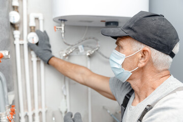 Male plumber in medical mask checks pipes for central hot and cold water supply of apartment