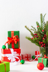 Red and green gift boxes and balls , fir tree branches and hawthorn twigs in a vase on white wall background, new year and christmas concept