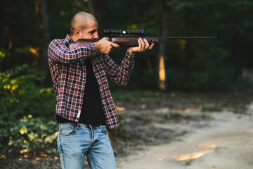 Charismatic guy in a checkered shirt with a weapon. In the autumn forest. Home protection alone