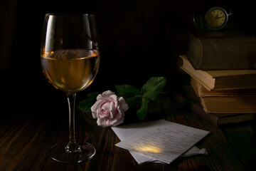 The photo shows a glass of wine with a letter and a rose on a dark background with books and a clock.