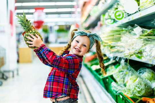 little kid standing with pineapple in supermarket