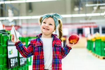 Cute little girl making list of goods to buy in supermarket