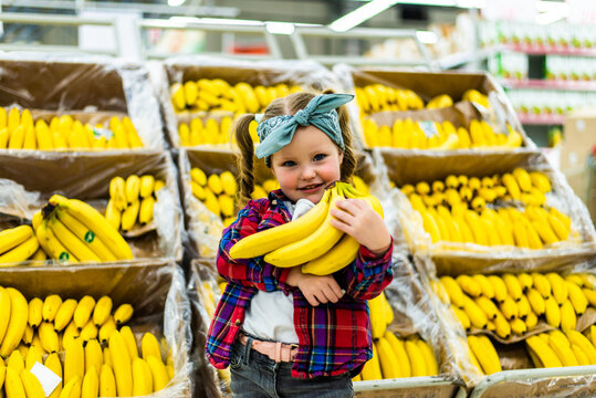 Cute little girl holding bananas in a food store supermarket