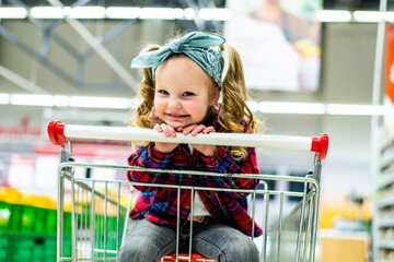Funny little girl sitting in the trolley during family shopping in hypermarket