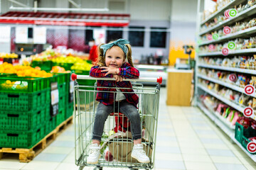 Adorable baby kid with trolley choosing fresh vegetables in local store. sale, consumerism and people concept