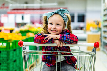 Funny little girl sitting in the trolley during family shopping in hypermarket