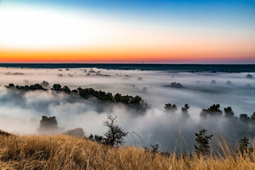 Beautiful panoramic landscape with river valley covered by thick fog in autumn in the early morning. Sunrise.