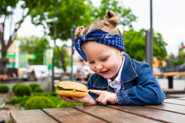 Little cute girl eating a burger in a cafe. Concept of a children's fast food meal