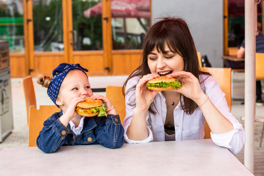 Mom And Daughter Eating Tasty Burgers In Fast Food Cafe