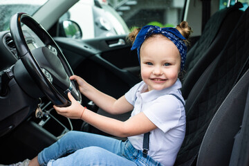 Happy little girl sitting of car on driver seat holding steering wheel
