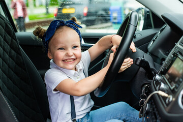 Little girl sitting in the car and holding the steering wheel