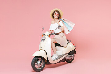 Fototapeta na wymiar Full length portrait of smiling young woman in white clothes hat glasses hold package bag with purchases after shopping looking camera driving moped isolated on pastel pink colour background studio.