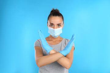 Woman in protective mask showing stop gesture on light blue background. Prevent spreading of COVID‑19