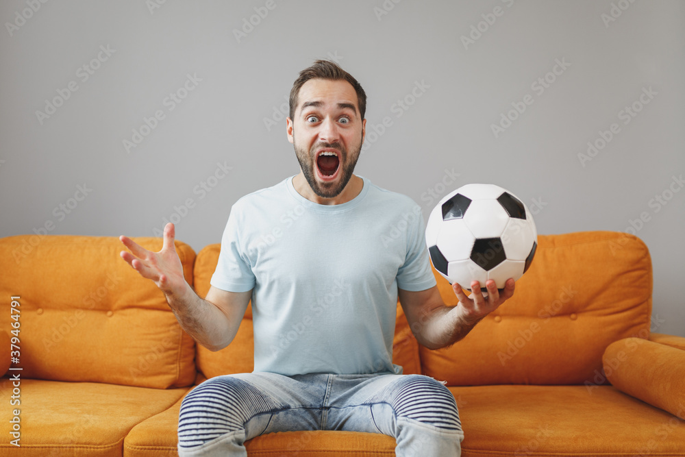 Wall mural shocked worried young bearded man football fan 20s in basic blue t-shirt cheer up support favorite t