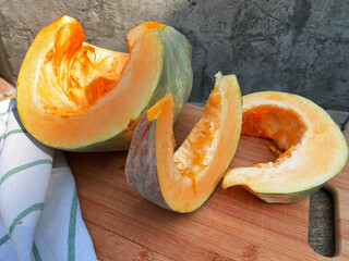 Ripe pumpkin cut into slices on a wooden cutting board, concrete background, autumn atmosphere