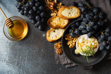 Roast camembert and honey with black grapes and baked slice of bread on dark background