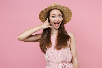 Excited young brunette woman 20s wearing pink summer dotted dress hat posing doing phone gesture like says call me back looking camera isolated on pastel pink color wall background studio portrait.