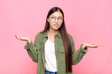 asian young woman shrugging with a dumb, crazy, confused, puzzled expression, feeling annoyed and...