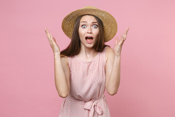 Shocked worried irritated young brunette woman 20s wearing pink summer dotted dress hat posing spreading hands swearing keeping mouth open isolated on pastel pink color background studio portrait.